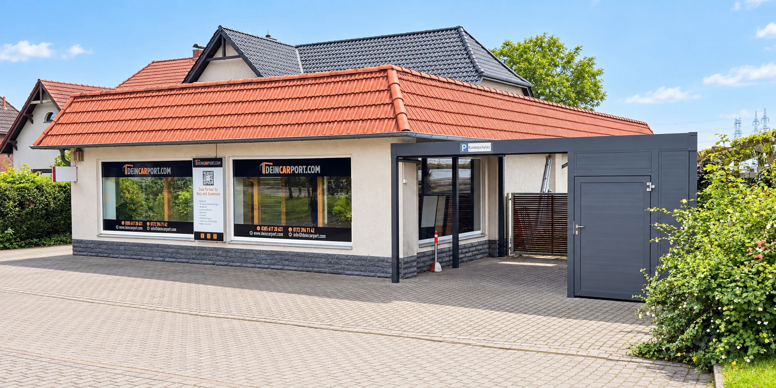 Ausstellung Außenansicht – Sommer Sommerliche Außenansicht der DeinCarport.com-Ausstellung mit Schaufenstern, Eingang und Kundenparkplatz.